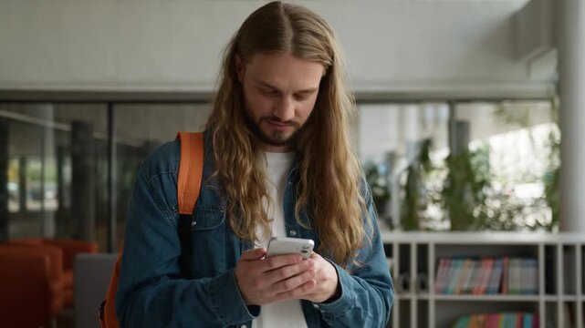 Caucasian man looking in mobile phone smiling cheerful chatting reading good news notification male student guy with smartphone smile laugh gadget messaging pleasant communication online in university