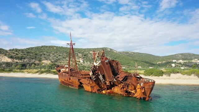 Aerial view of the rusted Dimitrios shipwreck resting in shallow turquoise waters near a sandy beach and green hills close to Gythio, Greece.