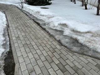 Fototapeta premium Paving stone sidewalk with melting dirty snow on the sides
