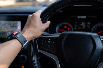 Obraz premium Close-up of Man Hand on Steering Wheel Driving Car with GPS Navigation and Smart Watch,A close-up, first-person perspective of a man's hand holding a leather steering wheel while driving.