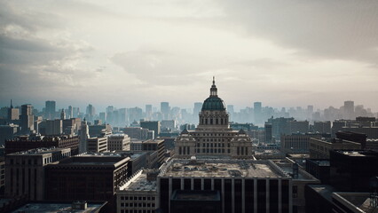 Obraz premium domed capitol building in morning haze, wide aerial vista of classical columns and stone facade, distant skyline under soft light, civic planner inspecting
