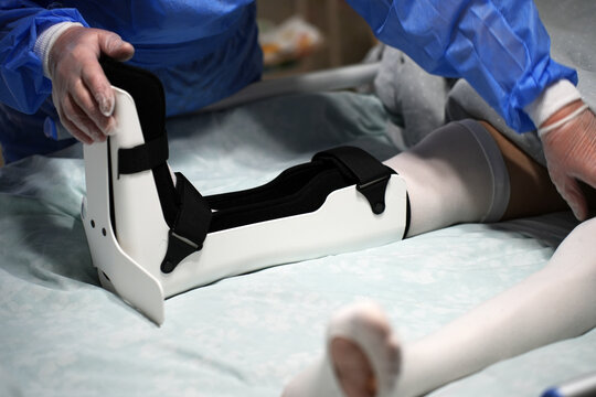 Medical Professional Adjusting Ankle Orthosis Brace. Doctor carefully correcting the fit of a orthopedic ankle foot orthosis (AFO) for a patient in a hospital bed. Focused on clinical rehabilitation