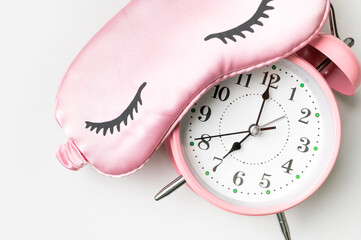 Pink sleep mask and pink alarm clock on light gray background flat lay top view. Concept for sound...