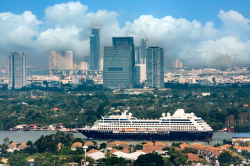 A passenger cruise ship navigates Chao Phraya River in Bangkok, Thailand, passing lush riverbanks and residential homes © aapsky