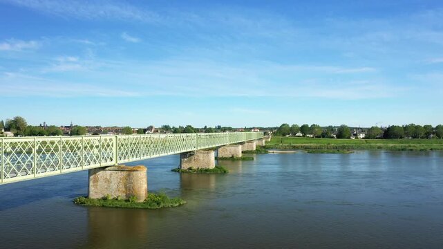 Scenic view of an iron bridge crossing the Loire River in Sully sur Loire, France, under a clear blue sky. Lush greenery and the town are visible in the background.