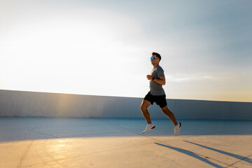 Man runs on a rooftop during sunset, enjoying fitness and outdoor activity in a city setting with clear skies above