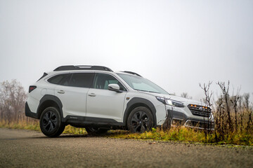 Naklejka premium Brno, Czech Republic - November 12, 2025: White Subaru Outback family car driving from field to road in autumn in fog outdoors. Japanese off-road SUV.