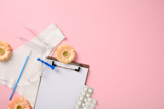 Medical flat lay for women's health featuring a plastic speculum, clipboard, and pills on a pink surface with gerbera flowers. Diagnostic and routine exam theme.
