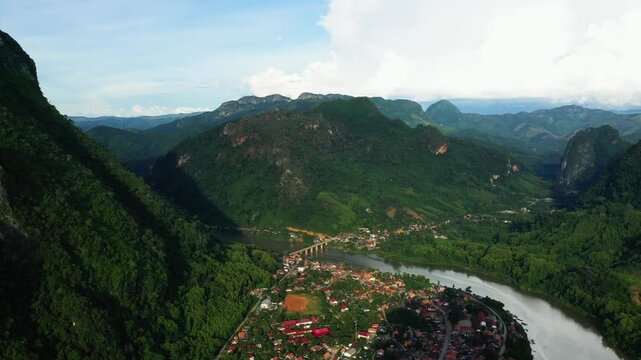 Scenic aerial shot of Nong Khiaw village nestled between lush green mountains with a winding river and bridge in northern Laos.