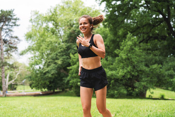 Naklejka premium Fit female jogger exercising in green park in summer morning.