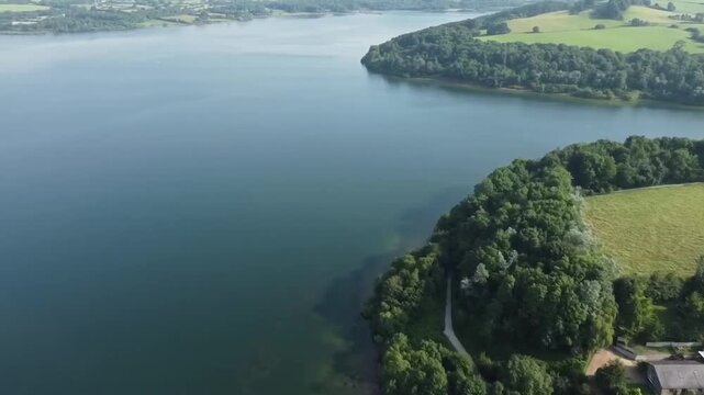 Aerial Drone Flight Over Carsington Water Shoreline with Green Fields Trees and Country House Derbyshire