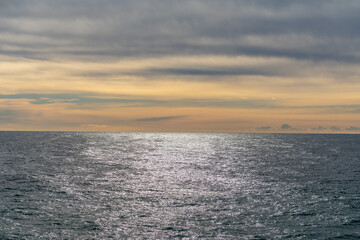 Fototapeta premium Ocean water glistening under a vast sky featuring a horizon line separating the deep blue sea from soft yellow and gray clouds, evoking a sense of tranquility and space
