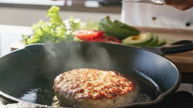 Close-up of a juicy burger patty sizzling in a cast-iron skillet, with fresh lettuce, tomato, and avocado slices in the background