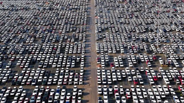 Aerial drone view of thousands of new cars parked in symmetrical rows at the massive vehicle import and export storage terminal in Grimsby, UK.