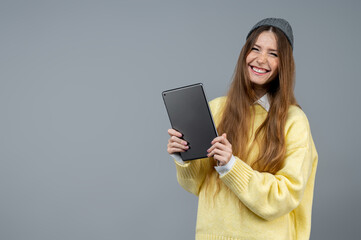 Young woman in casual clothes on a grey background with a tablet in hands