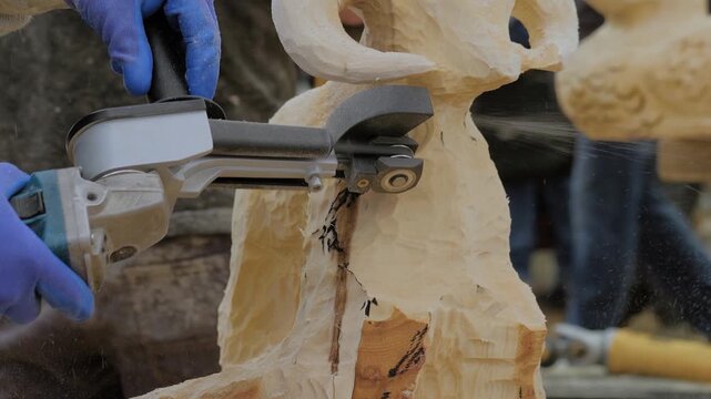 Man carpenter, wood sculptor using angle grinder with multi cutter disk saw attachment for carving wooden sculpture of goat - close up. Carpentry, hobby, craftsmanship and woodworking concept