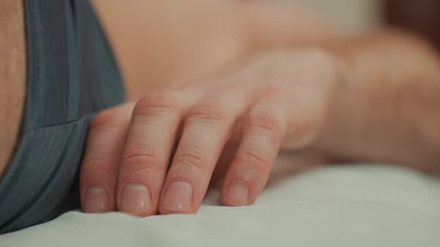 closeup hand resting on massage bed, male client awaiting microcurrent treatment, fingers relaxed on white linen, soft ambient lighting, clinical calm, shallow depth of field focusing on fingertips