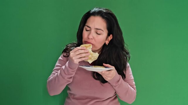 Middle-aged brunette woman with long hair savoring a delicious arepa. Her eyes are closed in enjoyment while she eats against a green screen