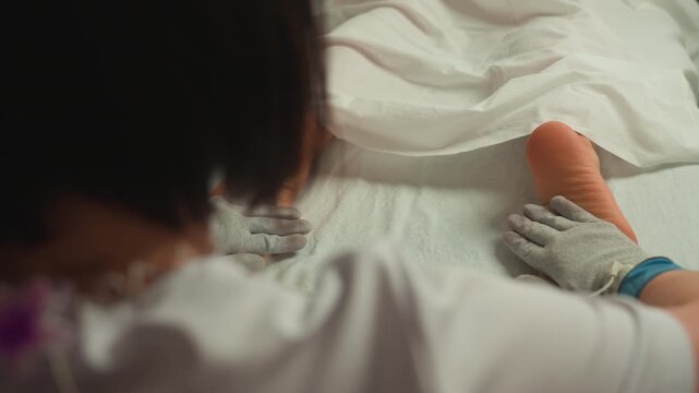 therapist performing microcurrent foot massage, gloved esthetician gently treats clients lower leg and foot on towelcovered bed with electrode device, closeup of hands, soft lighting, clinical spa