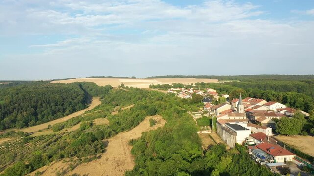 Drone shot of Hattonchatel village surrounded by lush green forests and golden agricultural fields under a blue sky. Picturesque rural landscape in northeastern France.