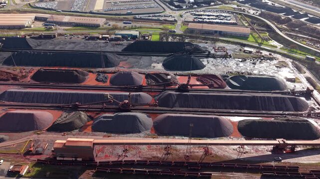 Aerial drone view of massive coal and iron ore stockpiles at Immingham Port, UK, featuring heavy industrial machinery and port operations.