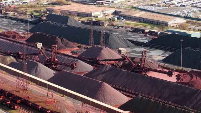 Aerial drone view of massive coal and iron ore stockpiles at Immingham Port, UK, featuring heavy industrial machinery and port operations.