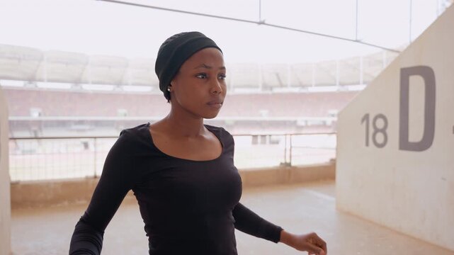 woman shadowboxing stadium corridor, throwing controlled punches with focused expression, pivoting footwork, concrete wall marked D, empty arena behind, highenergy training loop, breathy rhythm,