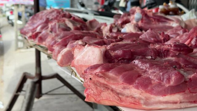Large portions of raw red meat lie across a vendor table in a traditional butcher stall, with surrounding market rows and food trade activity behind. Butcher stall.