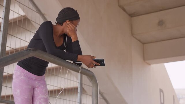 black woman leaning on railing, visibly exhausted and reflective with phone in hand, downward gaze and slumped posture, urban stairwell and concrete backdrop, muted palette, quiet solitude, creative