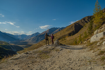 Fototapeta premium Couple of hikers with backpacks giving high five on mountain edge overlooking scenic alpine valley during autumn trekking trip for teamwork, success and travel adventure concept. 