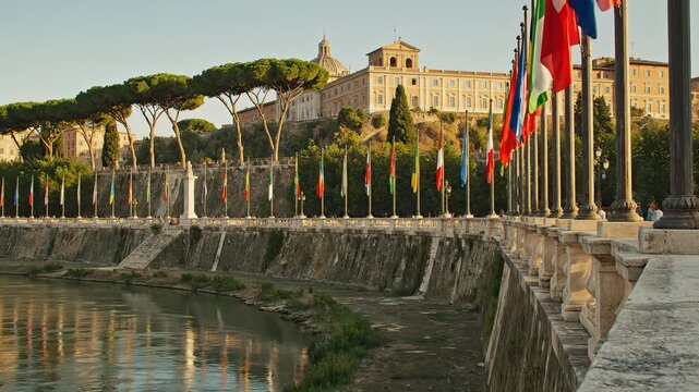 Row of National Flags Fluttering in the Wind with a Historic Building and Lush Greenery Reflected in Water.