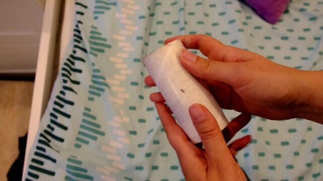 Close up shows hands peeling off a used lint roller sheet covered with hair and dust, bed linen blurred behind. Removing allergens supports cleaner air, better sleep, and healthier routines at home.