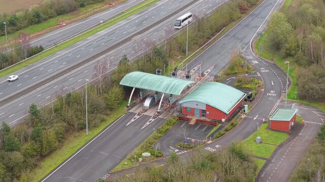 Aerial drone view of the M6 Toll motorway and its automated payment booths, with HGVs and commuter vehicles passing through near Birmingham, UK.