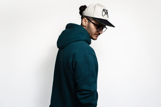 Studio profile portrait of young man wearing eyeglasses, cap and hoodie sweater.