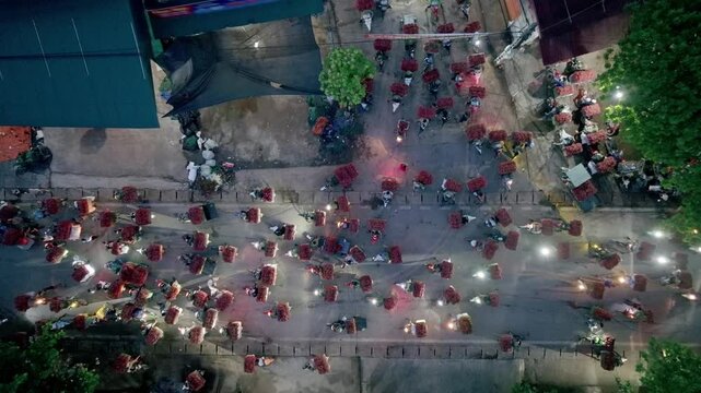 Aerial night view of motorbikes and carts loaded with lychee moving along a village road in Lục Ngạn during peak harvest season.