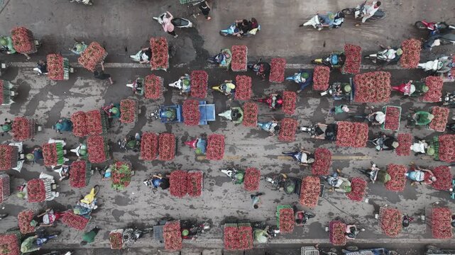 Top-down aerial view of densely packed motorbikes carrying baskets of freshly harvested lychee along a narrow rural road.