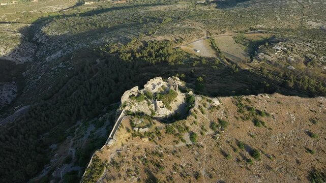 Drone shot of the ancient ruins of Chateau de Opoul Perillos surrounded by rugged landscape in southern France. The historic stone structure stands atop a hill with panoramic views of the countryside.