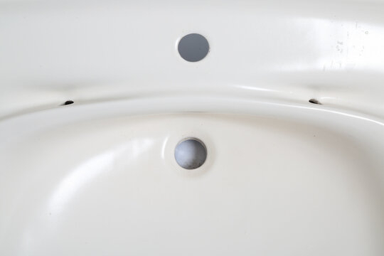 Close-up view of a white ceramic sink with two drainage holes and small imperfections