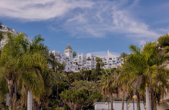 Whitewashed buildings cascade down a hillside surrounded by lush palm trees under a blue sky