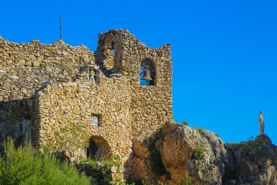Ancient stone chapel surrounded by greenery against a bright blue sky