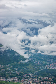 Panoramic view over Merano and the Burgraviato in the Adige Valley; Vinschgau (Val Venosta) and the Oetztal Alps with dramatic low clouds against snowcapped mountains in South Tyrol, Italy