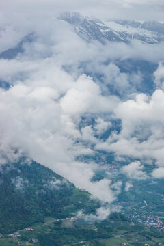 Panoramic view over the Burgraviato in the Adige Valley; Vinschgau (Val Venosta) and the Oetztal Alps with dramatic low clouds against snowcapped mountains in South Tyrol, Italy