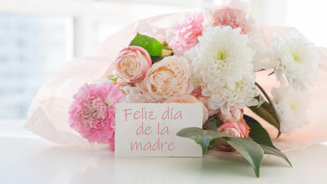 bouquet of pink roses, white chrysanthemums and soft carnation with green leaves and greeting card with text happy mothers day in spanish - feliz dia de la madre, perfect for mothers day celebration