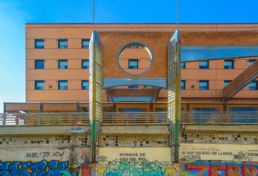Modern building with circular window and graffiti on lower wall under blue sky