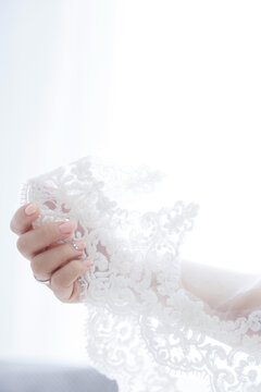 Delicate white lace held by a manicured hand with a wedding ring and subtle gems