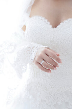 Close-up of a bride's hand wearing a diamond wedding ring on her lace-covered dress