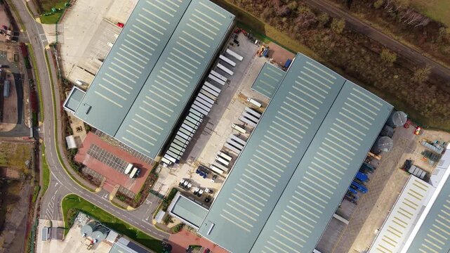 Top-down aerial drone view of a large distribution centre in Birmingham, UK, featuring rows of HGVs waiting at busy warehouse loading bays.
