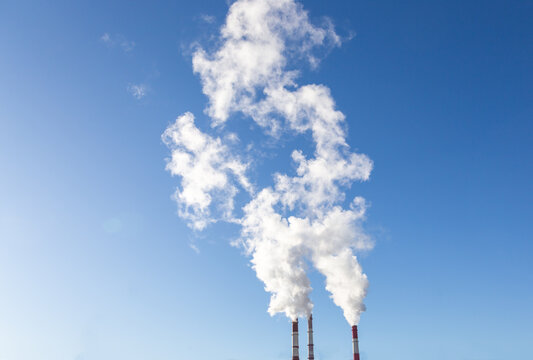 CHP emissions. Smoking chimney releasing smoke against a blue sky. Smoke from factory pipe of heat station in the city. Air pollution. Nuclear power plant cooling. CO2, greenhouse gases emissions.