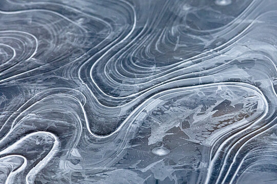 Layered bands sweep over a sheet of frozen water tracing soft pathways that curl and meet. The wintry surface becomes living art where graceful contours and gentle rhythm invite calm.