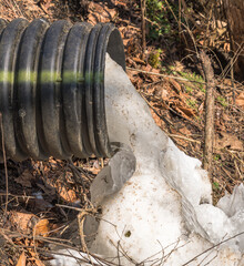 Obraz premium A corrugated drainage pipe discharging meltwater and ice into a small creek in in Warren County, Pennsylvania, USA on a sunny winter day